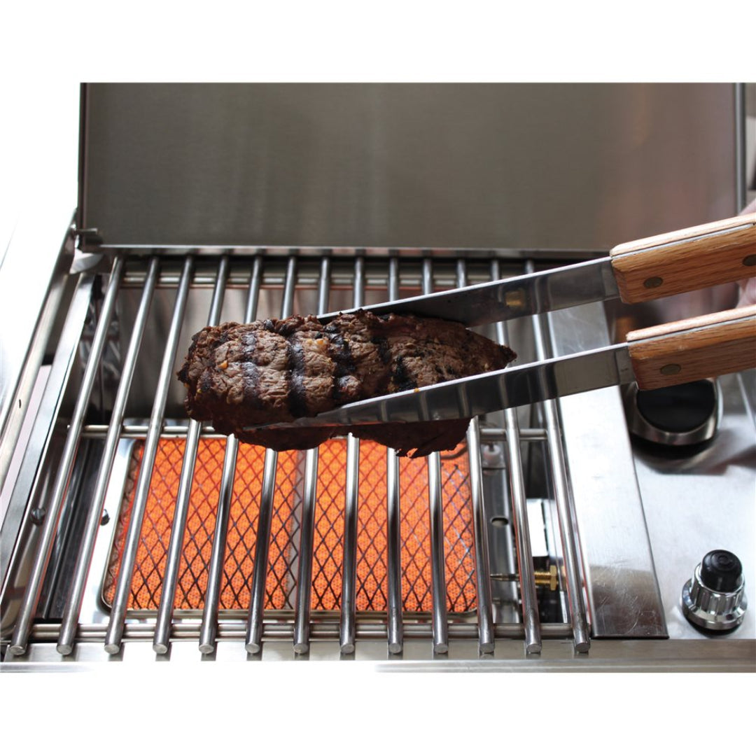 Vine & Flame DPA151 stainless steel built-in gas grill with glowing ceramic infrared sear plate, stainless grates and wood-handled tongs holding a charred grilled steak