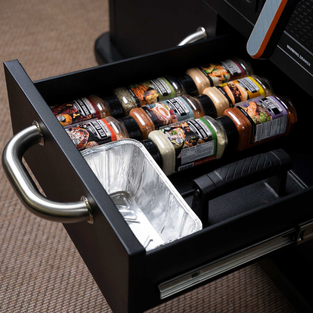 36-inch patio 4-burner air fryer combo grill warming drawer open showing organized spice jars, disposable aluminum drip pan and stainless drawer handle