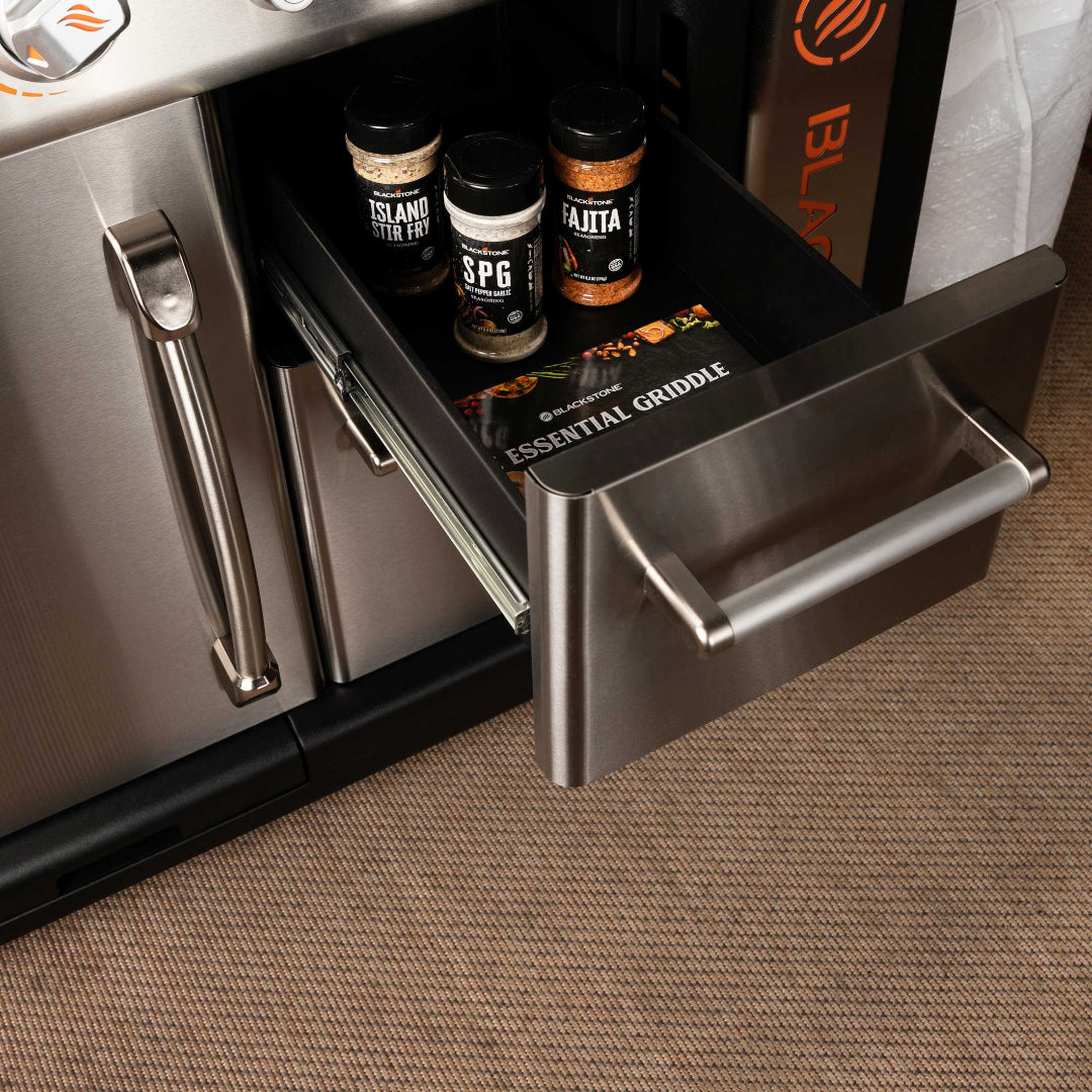Blackstone 36-inch Patio Pro outdoor griddle stainless-steel under-cart storage drawer open with seasoning jars (SPG, Island Stir Fry, Fajita) and Essential Griddle manual