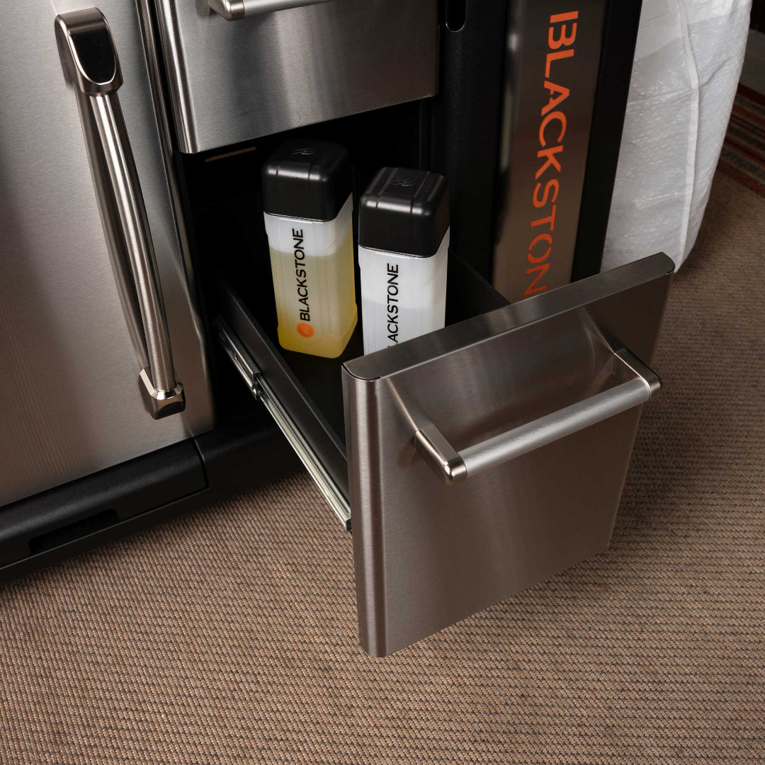 Blackstone 36-inch Patio Pro griddle stainless steel lower grease drawer open showing Blackstone oil and cleaning squeeze bottles for outdoor flat-top griddle storage
