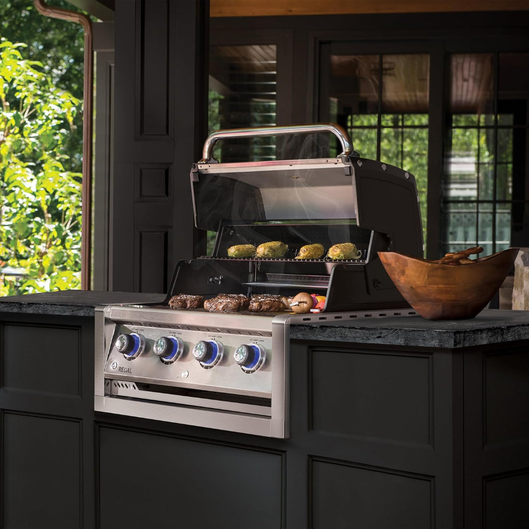 Built-in gas grill, Broil King Regal series, outdoor kitchen setup, blue LED knobs and open hood with food grilling
