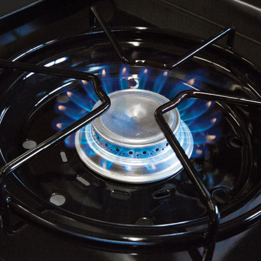 Broil King gas grill burner with blue flame and black cast iron grate, stainless steel cooking surface