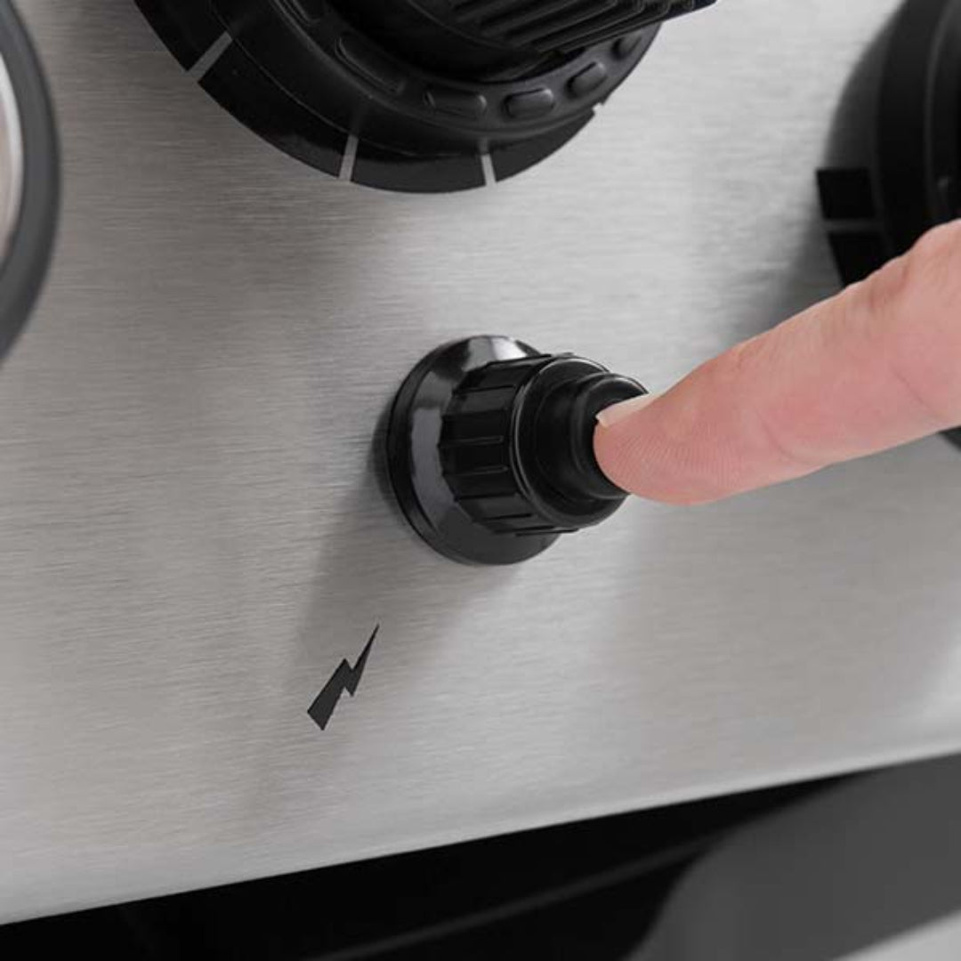 Broil King black push-button igniter knob on stainless steel grill control panel with finger pressing