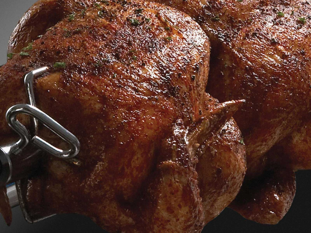 Broil King rotisserie chicken cooking on stainless steel spit rod with meat forks