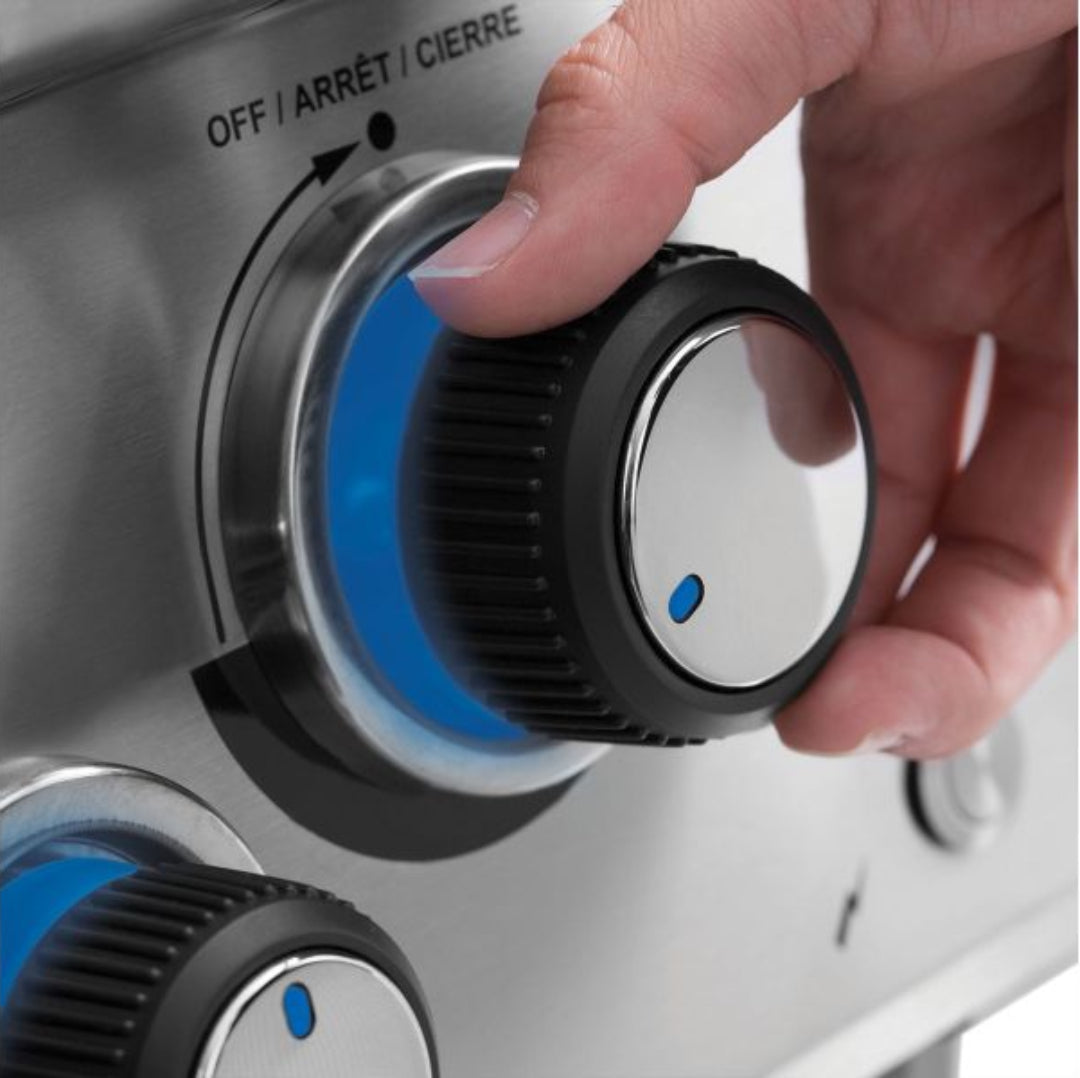 Close-up of hand turning illuminated blue control knob on Broil King grill.