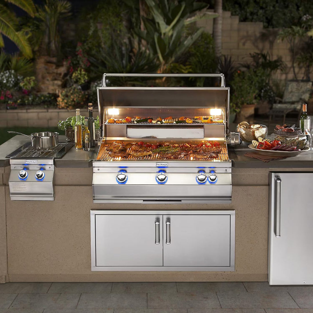Fire Magic A660i built-in stainless steel 4-burner gas grill with side burner, LED control knobs, warming rack and interior lights in outdoor kitchen island