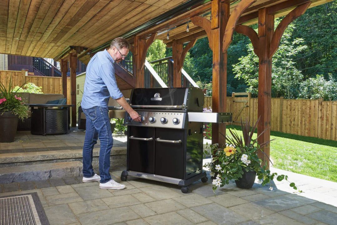 Outdoor kitchen scene, Broil King, Baron Series, 5-burner propane grill in use under wooden pergola with man grilling