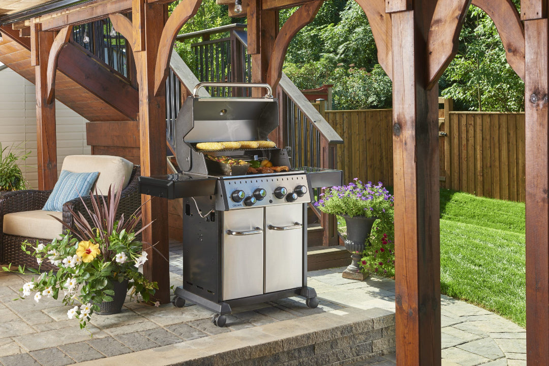 Freestanding grill, Broil King Crown, 4-burner propane, stainless cabinet, outdoor patio setup with food grilling