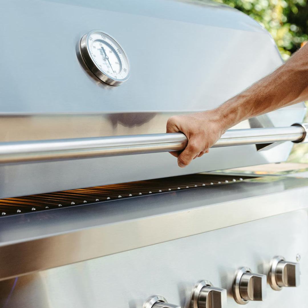 Man opening the lid of American Made Grills Encore 36-inch propane grill, showing temperature gauge and stainless steel control knobs