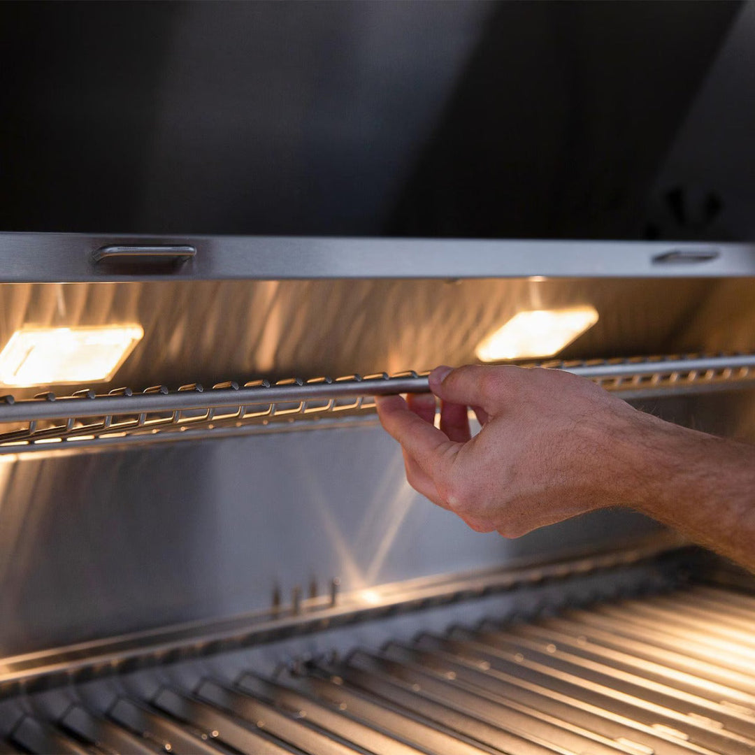 Hand adjusting warming rack inside American Made Grills Encore 54" natural gas grill with internal halogen lights