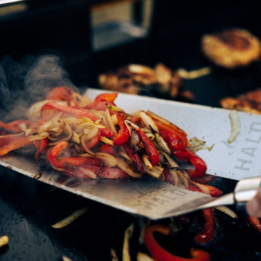 HALO HZ-3024 stainless steel scoop spatula lifting sizzling sautéed red bell peppers and onions on a hot griddle