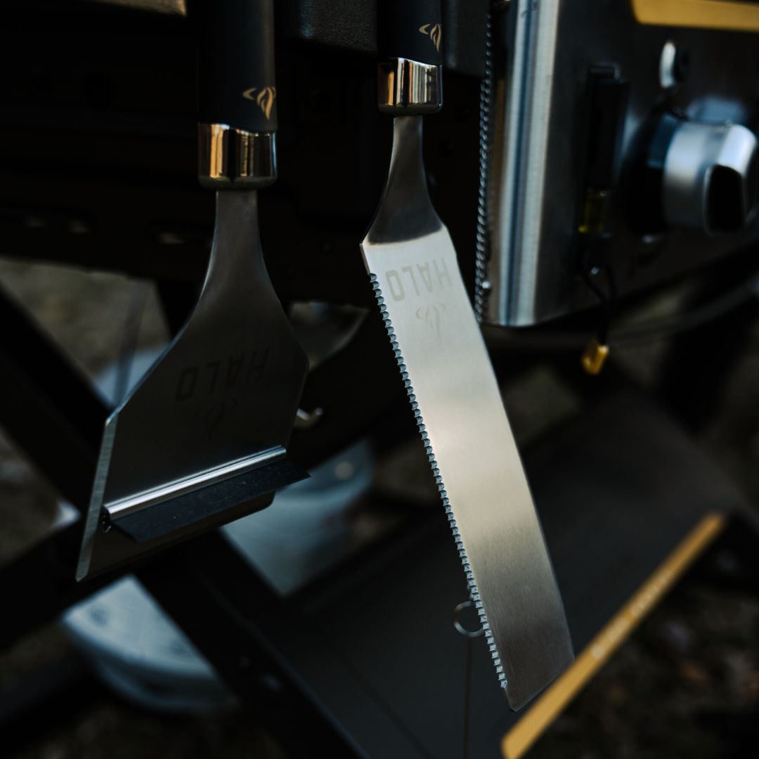 HALO HZ-3025 stainless-steel griddle tools — serrated blade spatula and squeegee scraper with magnetic handles hanging on a grill