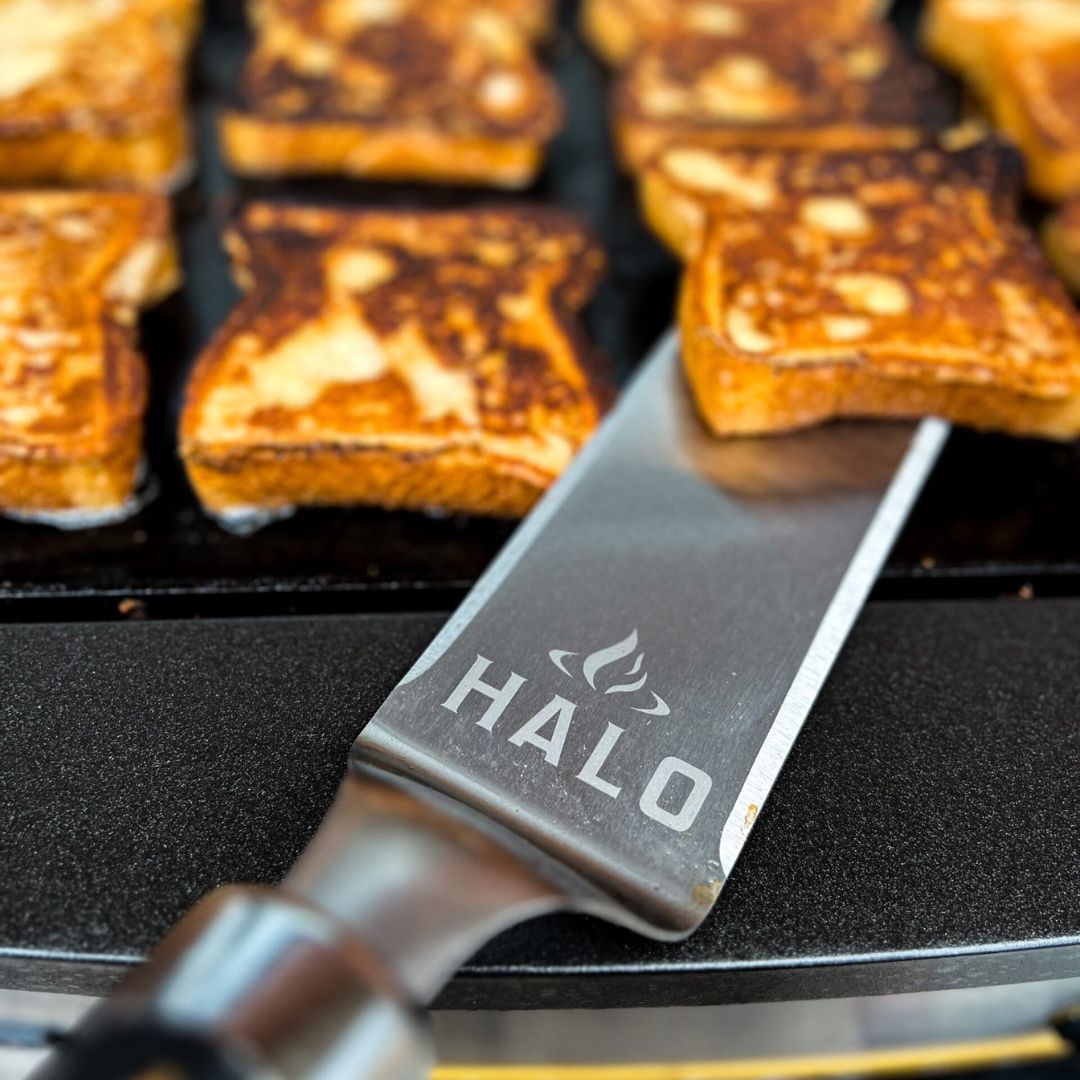 Close-up of HALO stainless-steel blade spatula (HZ-3025) lifting toasted sandwiches on a flat griddle.