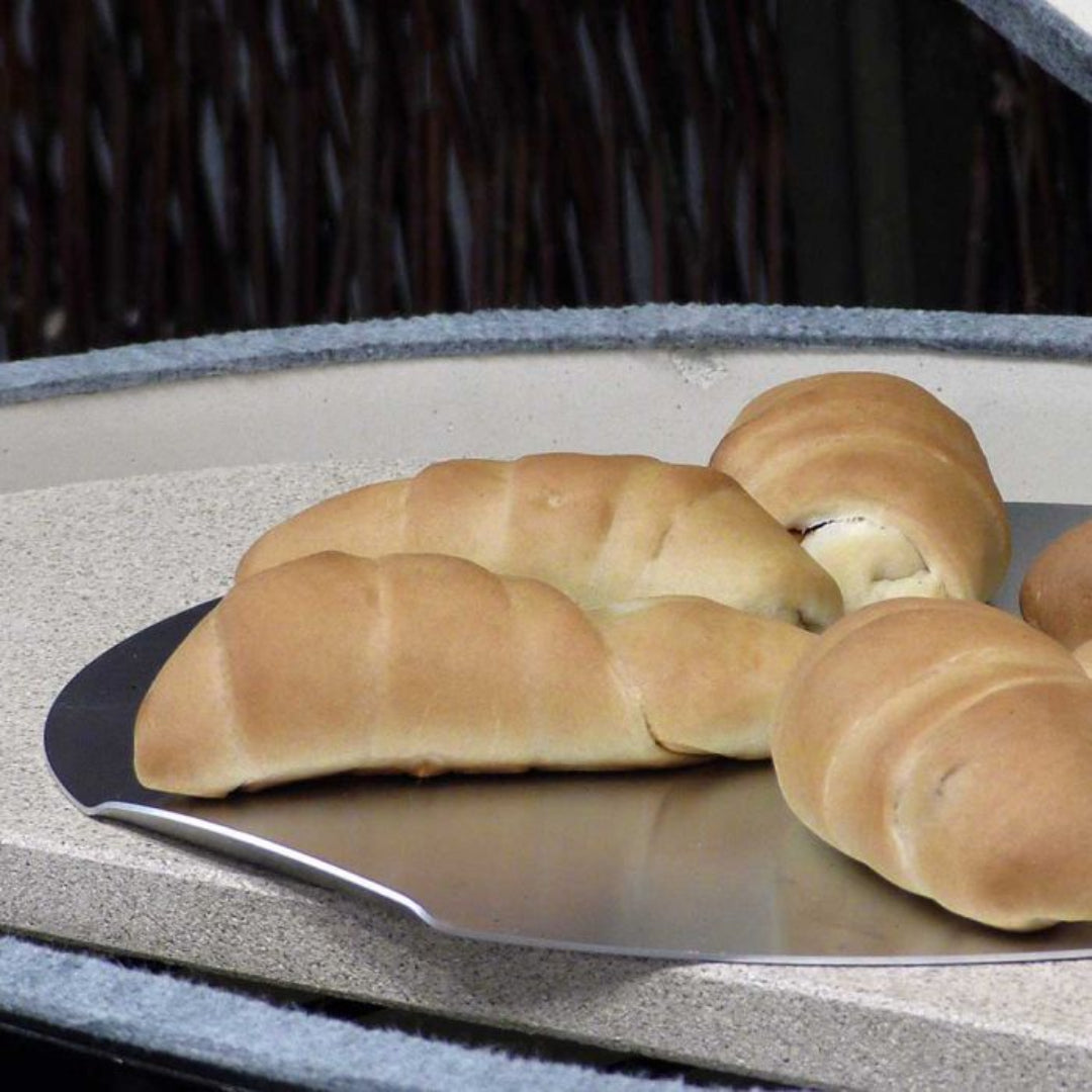Stainless steel pizza/baking peel on outdoor pizza oven stone holding freshly baked crescent rolls