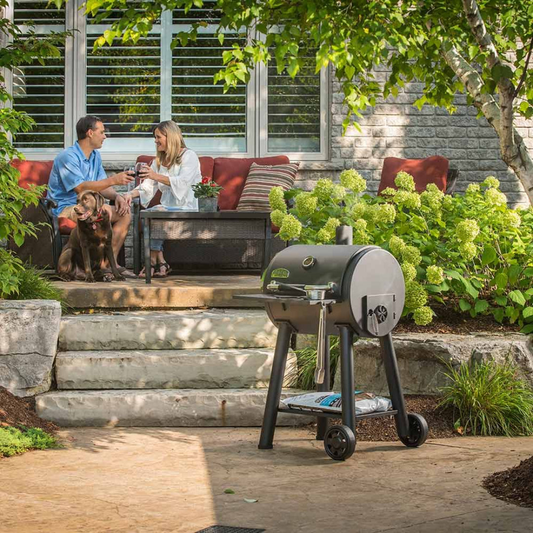 Charcoal grill, Broil King, Smoke Series, outdoor patio scene with couple and dog, relaxing with wine near blooming hydrangeas