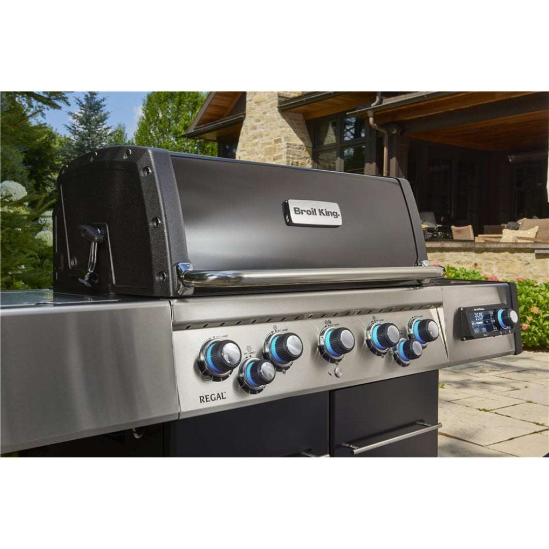 Broil King Regal 590 stainless steel 6-burner gas grill with LED-illuminated blue control knobs, digital temperature display and side shelf on outdoor patio
