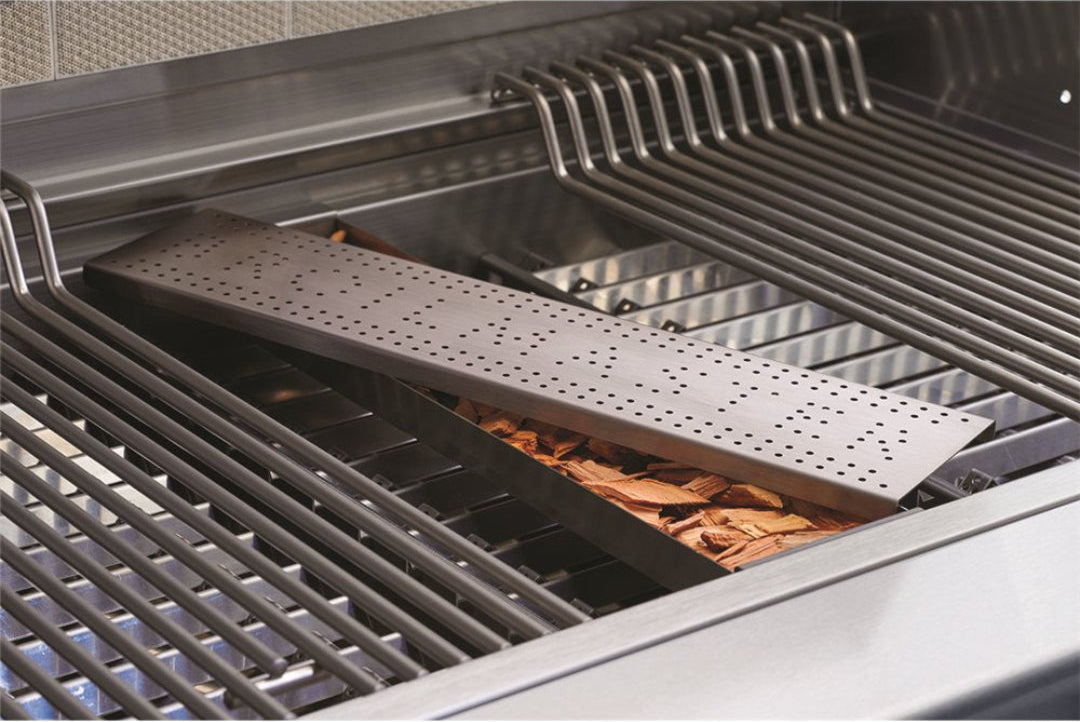 Stainless steel perforated wood chip smoker box for gas grill with wood chips fitted between cooking grates — heavy-duty grill smoking tray outdoor kitchen accessory