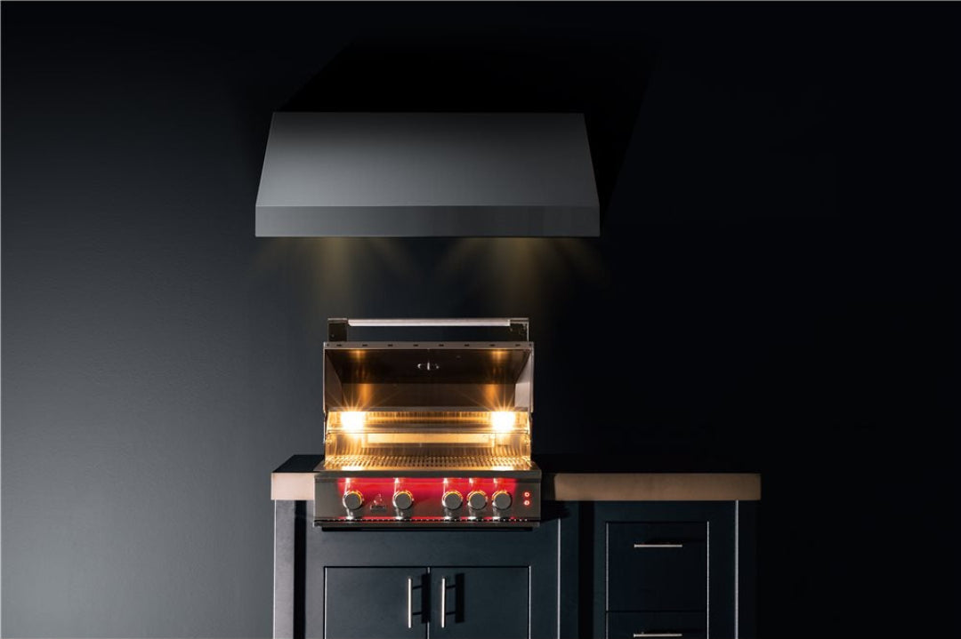Trueflame built-in stainless steel gas grill with vent hood and interior cooking lights, red four-knob control panel installed in dark outdoor kitchen island, Vine and Flame