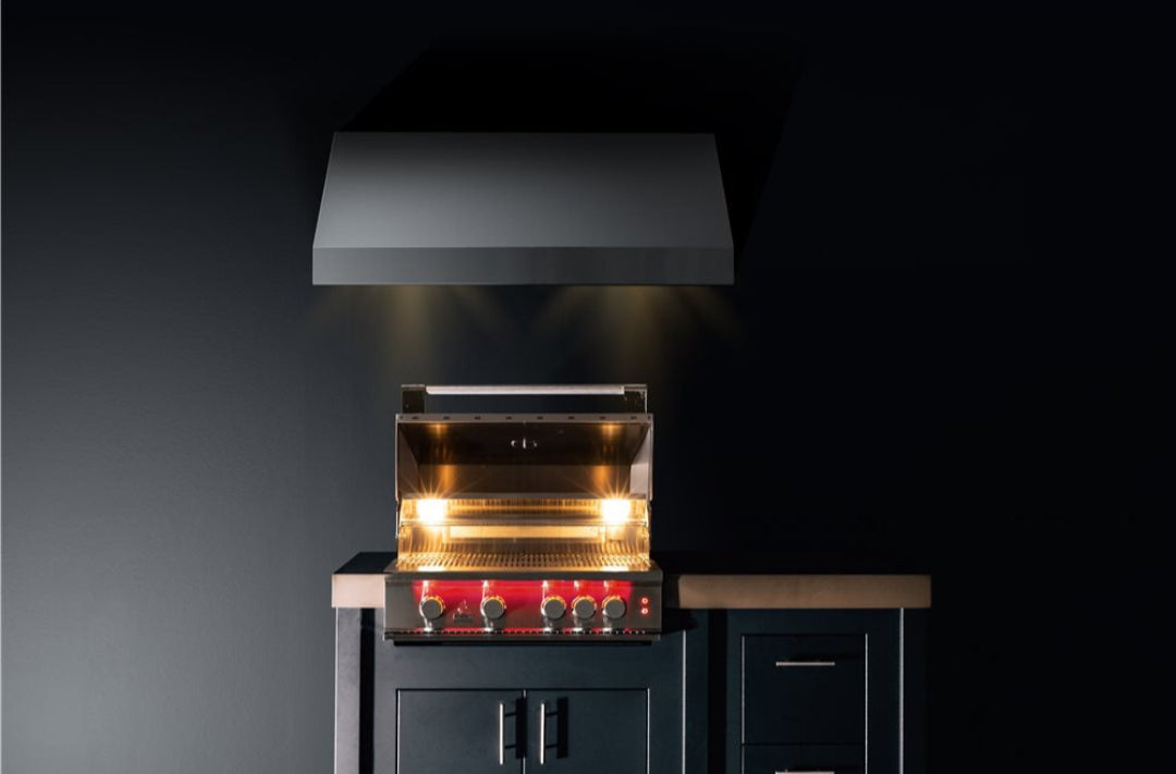 TrueFlame built-in 4-burner stainless steel gas grill with hood lighting and red control knobs under stainless vent hood in integrated outdoor kitchen island