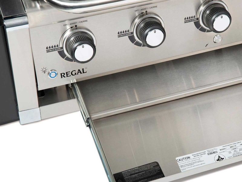 Broil King Regal series grill, close-up of control knobs and open drip tray, stainless steel build