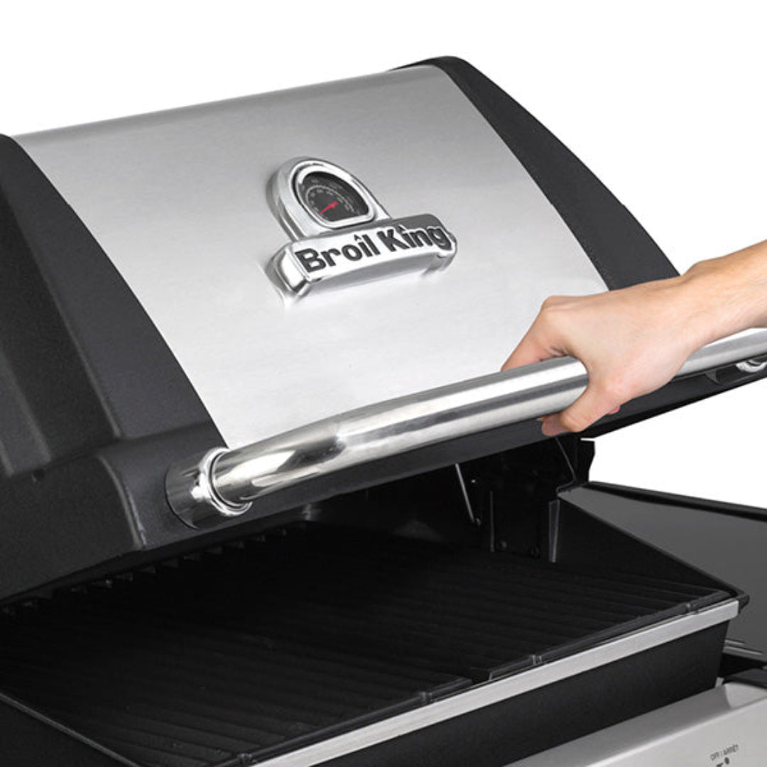 Broil King grill stainless steel lid with thermometer and handle being lifted by a hand to open grill hood