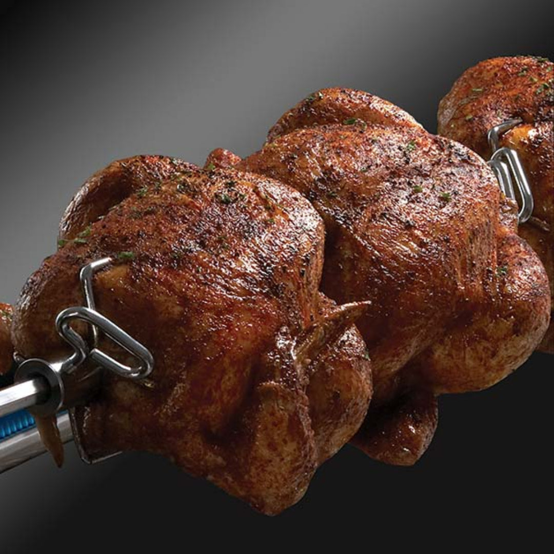 Broil King gas grill rotisserie spit with three whole seasoned chickens roasting on stainless steel grill