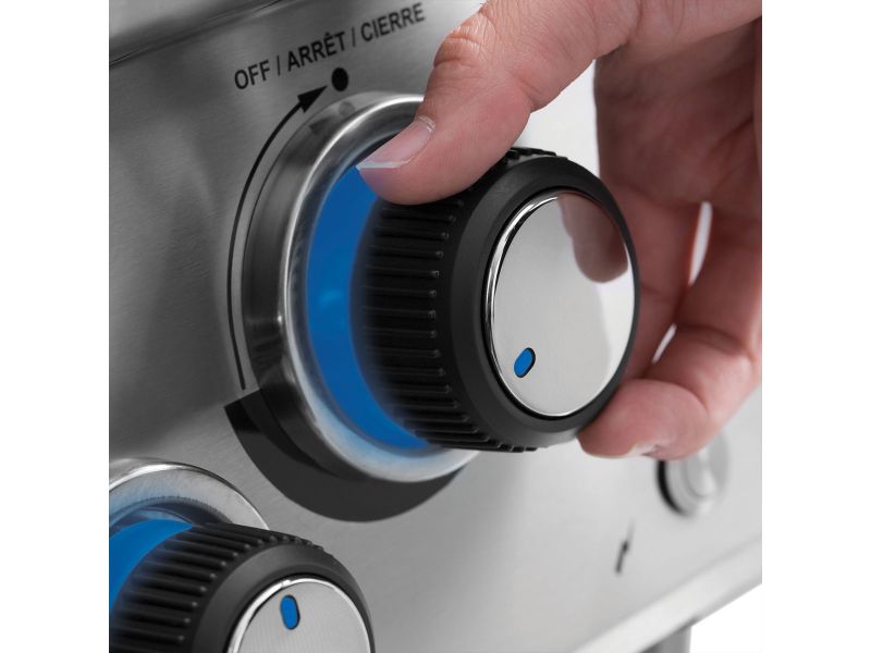 Close-up of hand turning illuminated blue control knob on Broil King grill.