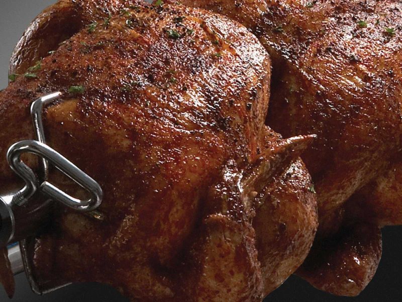Whole seasoned chickens cooking on Broil King rotisserie spit rod inside a gas grill.