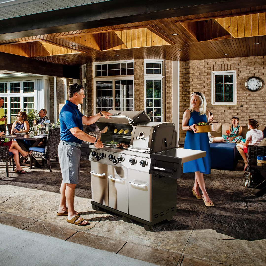 Broil King Regal S 690 Pro stainless steel gas grill on cart with three-door storage cabinet and side shelf on covered patio during backyard entertaining, outdoor kitchen — vineandflame.com