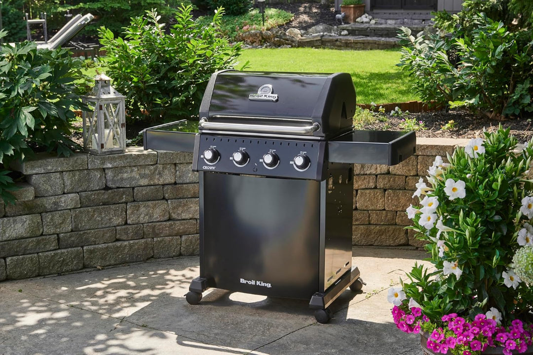 Freestanding grill, Broil King, Crown Series, outdoor patio scene with black 4-burner propane gas grill and side shelves
