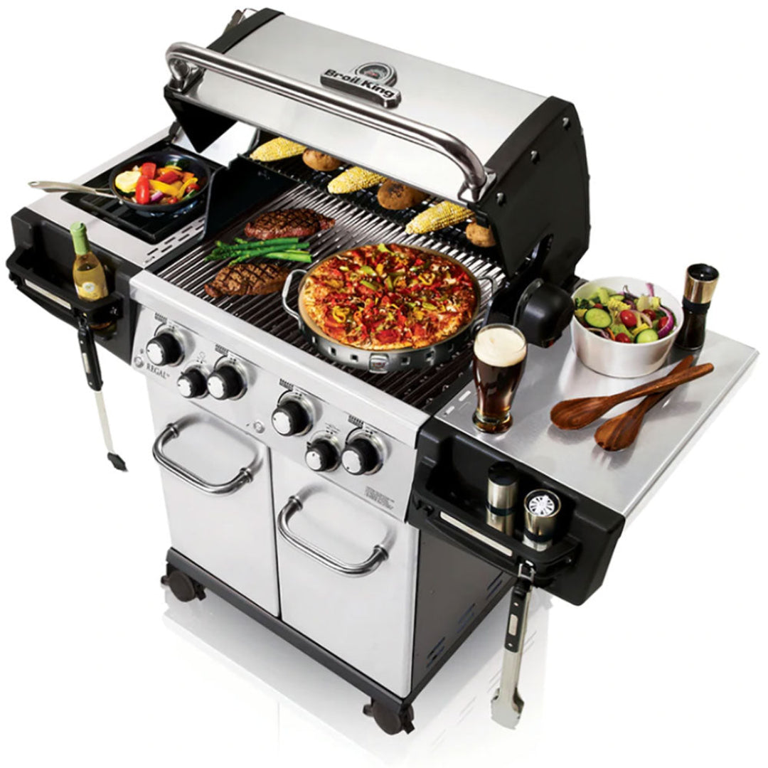 Broil King Regal S 490 Pro infrared natural gas freestanding 4-burner grill with iQue precision cooking, stainless steel cabinet cart and side shelves cooking pizza, steaks and corn