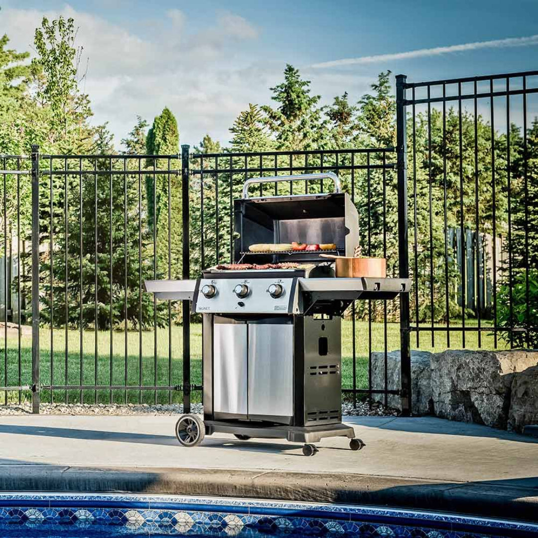 Gas grill, Broil King, Signet series, stainless steel front panel, open lid, grilling food by poolside, outdoor setting
