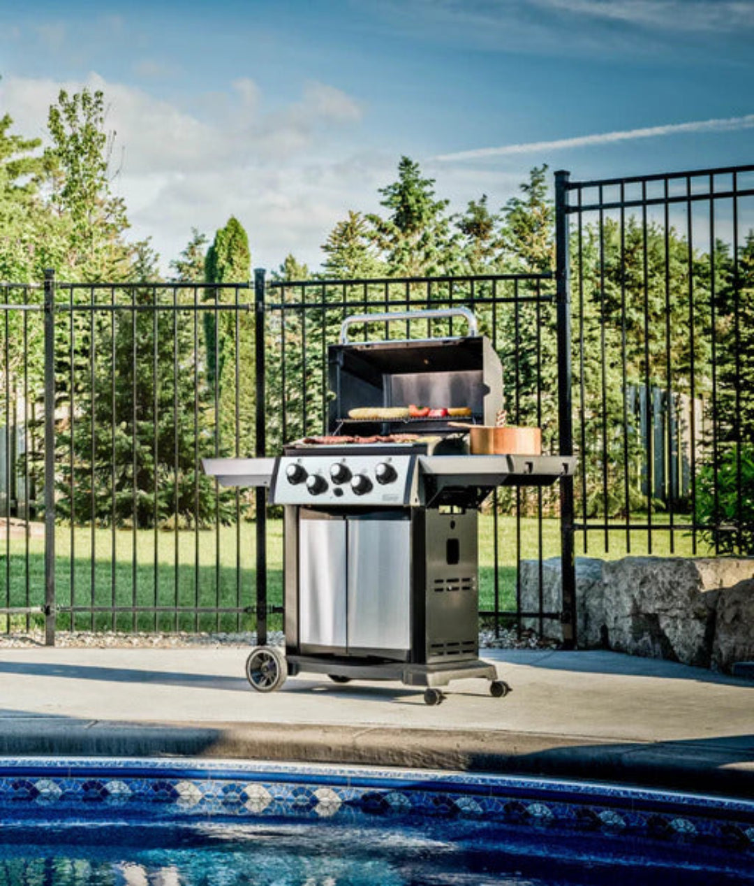 Gas grill, Broil King, Signet series, freestanding by the pool, outdoor lifestyle image with food on grates