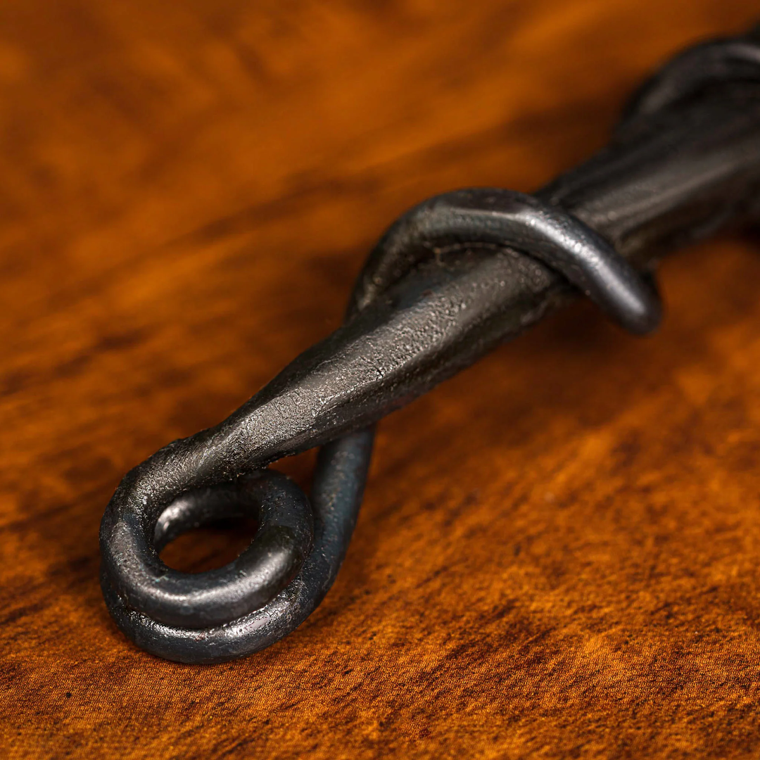 Cowboy Cauldron hand-forged bottle opener, rustic blacksmith forged iron loop and curled tip close-up on wood — Vine & Flame