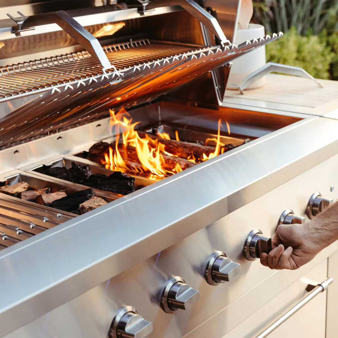Hand adjusting control knob on American Made Grills Encore 36-inch propane grill with open lid and active wood fire