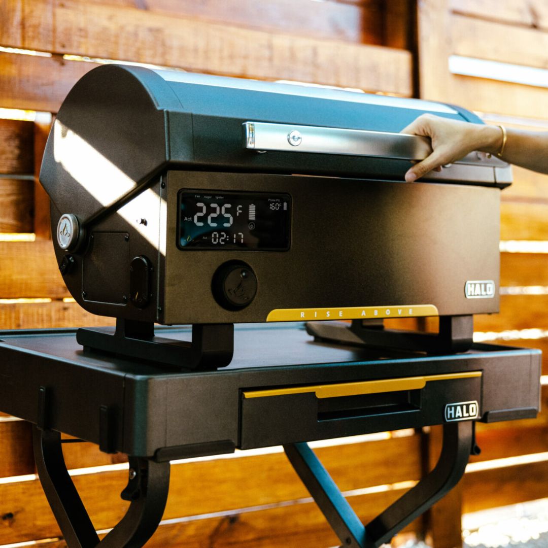 HALO Countertop Cart HO-1006-XNA black folding outdoor prep cart with drop-down drawer and swivel casters supporting a HALO countertop pizza oven, hand on oven handle