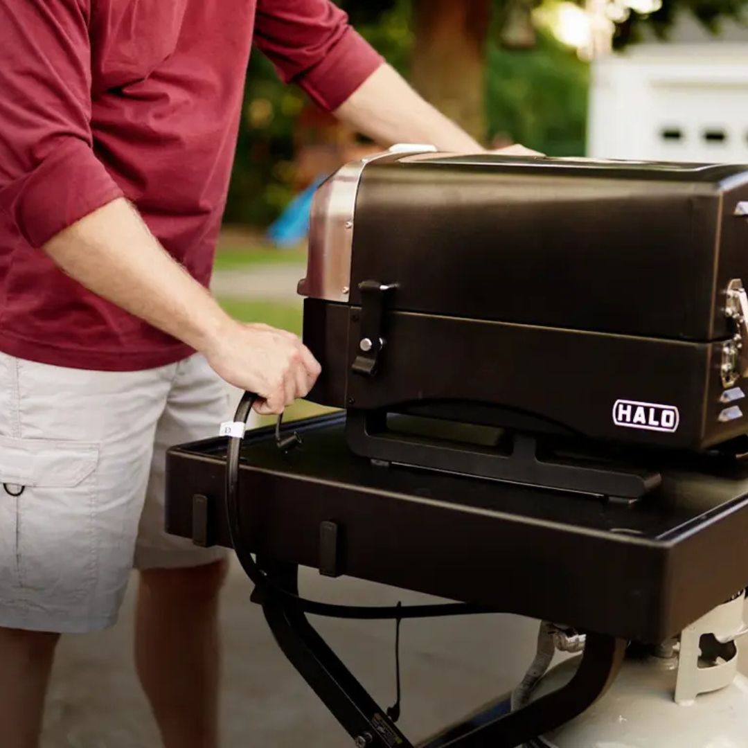 Black HALO Versa 16 portable 16-inch gas pizza oven (HZ-1004-ANA) on stand with person attaching propane hose