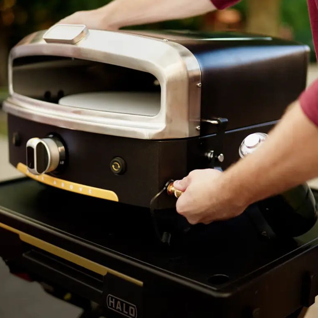 HALO Versa 16 outdoor gas pizza oven with 16-inch rotating cordierite stone and hands connecting propane canister