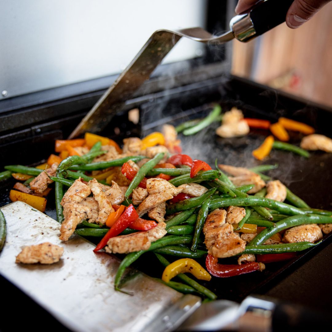HALO Elite 1B Griddle (HZ-1007-ANA) flat-top griddle cooking seasoned chicken, green beans and red and yellow bell peppers being flipped with a spatula