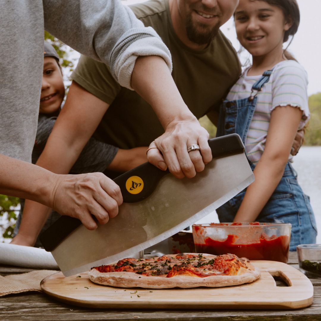 HALO HZ-3022 mezzaluna cutter slicing pizza on wooden board outdoors with family in the background