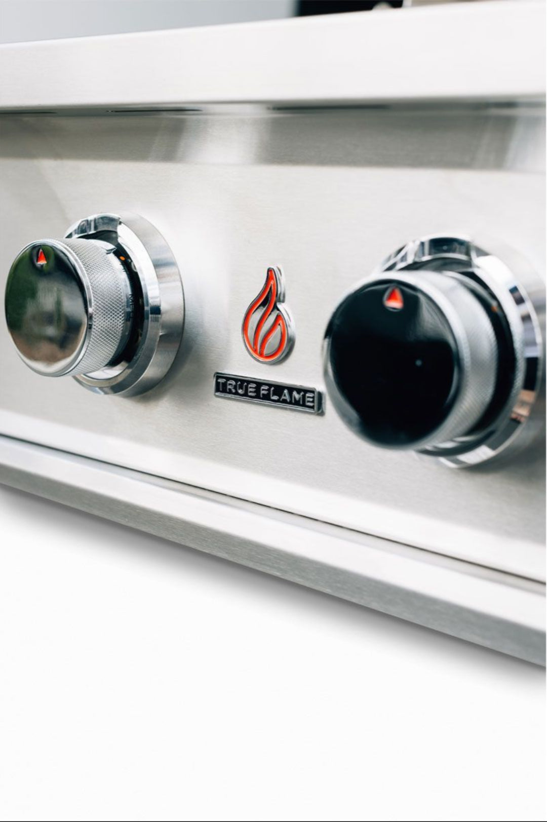 TrueFlame TFE25-NG stainless steel built-in natural gas grill close-up control panel with chrome knurled knobs and red flame emblem
