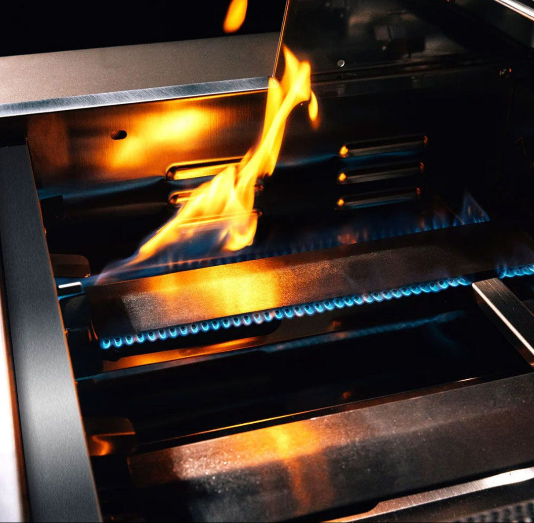 Close-up of stainless steel burners and heat shields with blue gas flame and orange sear flame inside TrueFlame TF Series 25-inch 3-burner built-in natural gas grill TF25-NG3