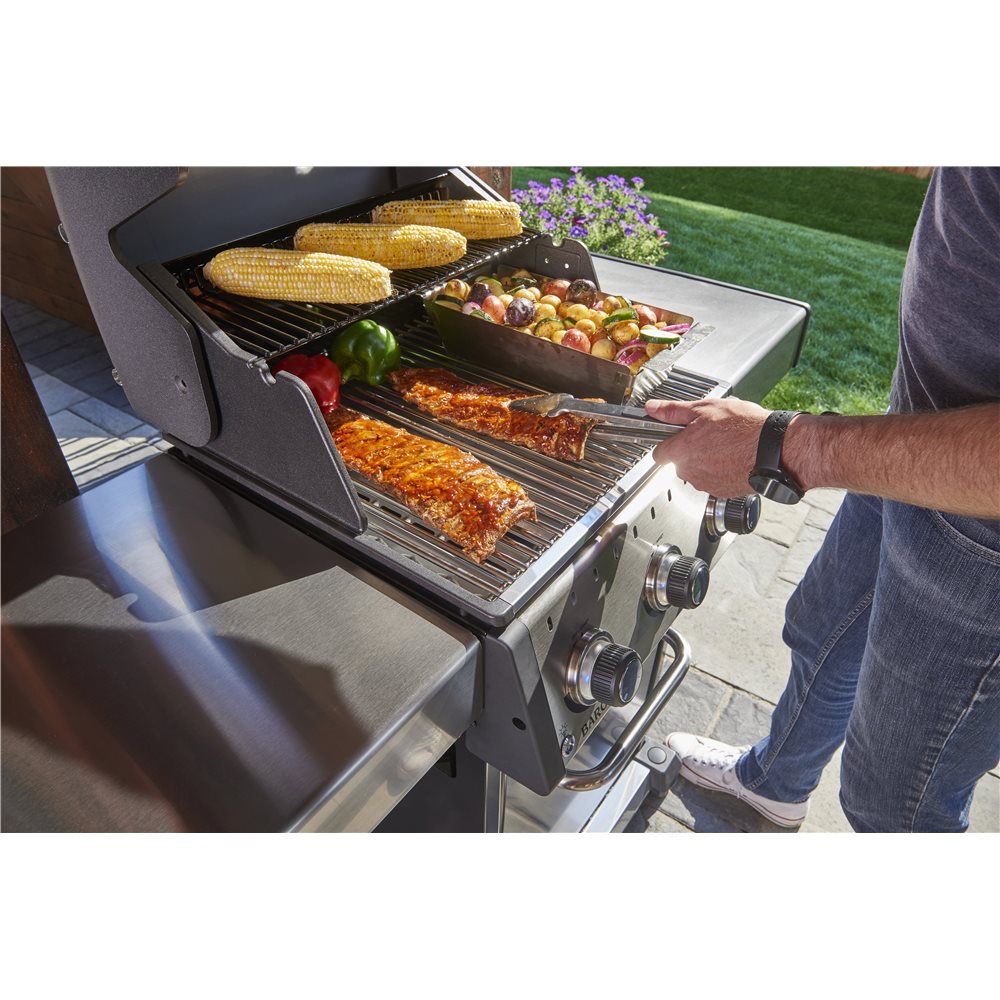 Freestanding grill, Broil King, Baron Series, grilling ribs, vegetables, and corn with open lid in backyard setting