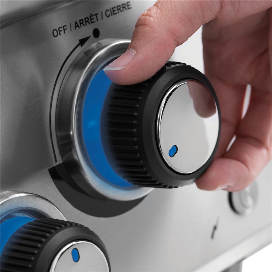 Close-up of hand turning stainless steel gas grill control knob with blue LED backlit control lights for outdoor propane BBQ